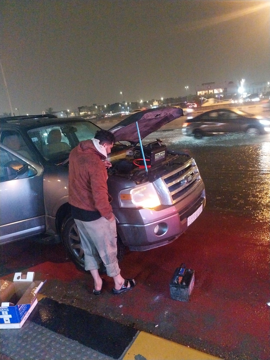فني يستبدل بطارية سيارة ليلاً على الطريق في الدمام